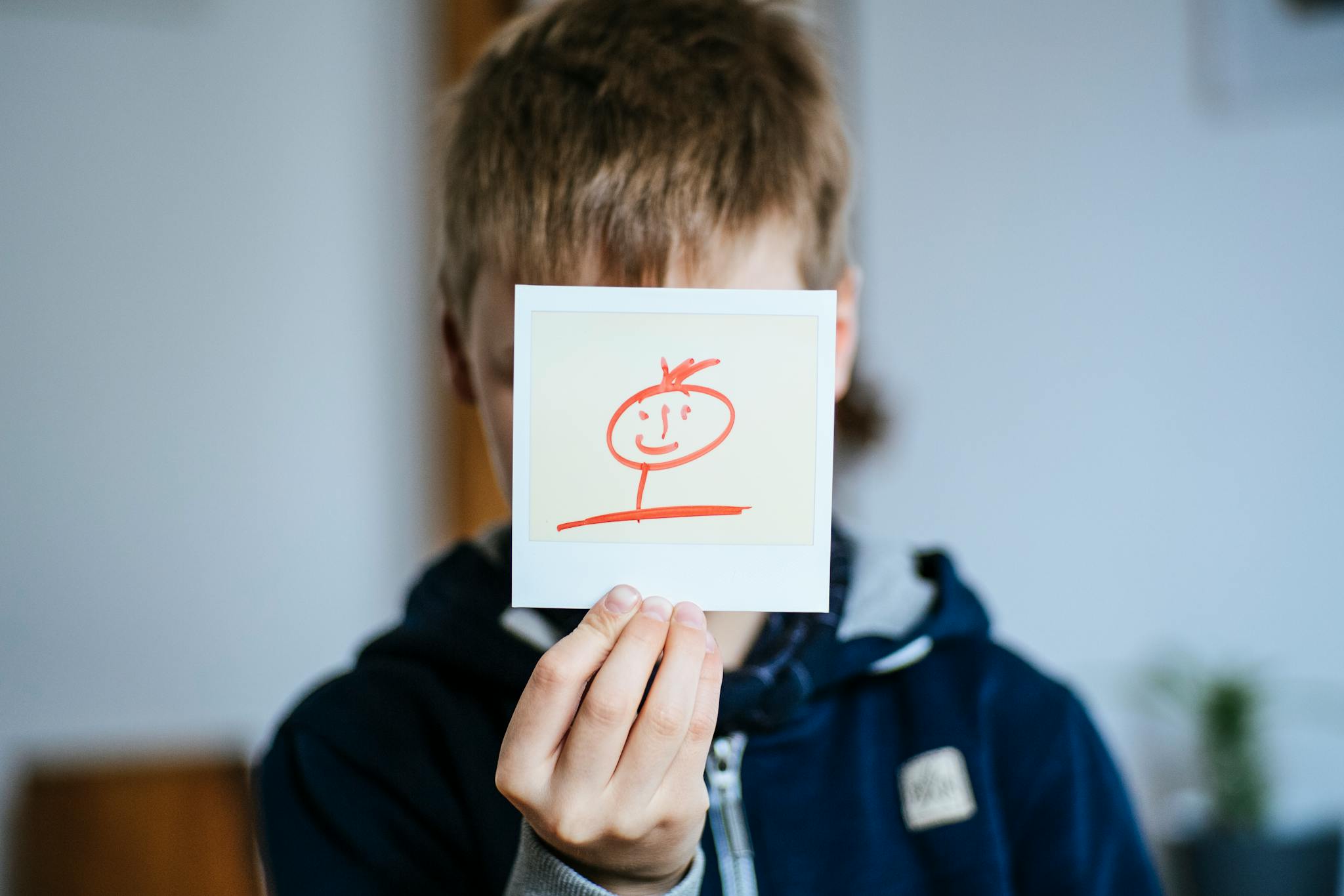 A child holding a hand-drawn stick figure portrait indoors.