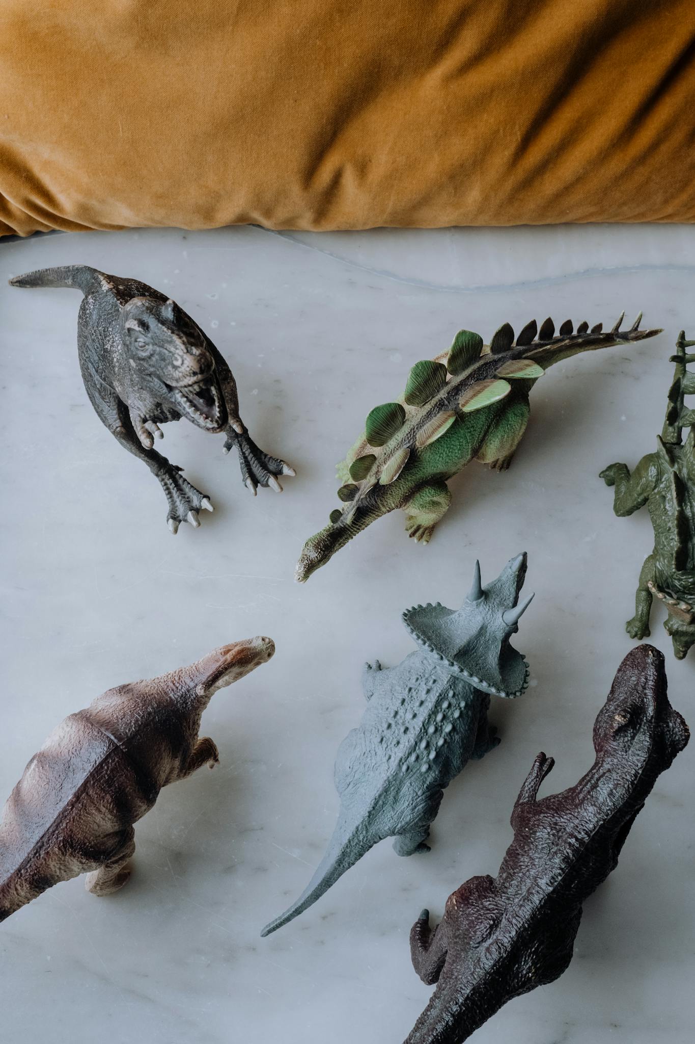 Top view of various dinosaur figurines arranged on a marble surface, showcasing a creative display.